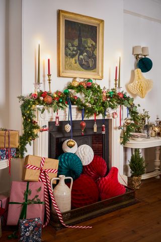 A fireplace with white mantel, framed wall art, festive foliage garland and various paper honeycomb decorations