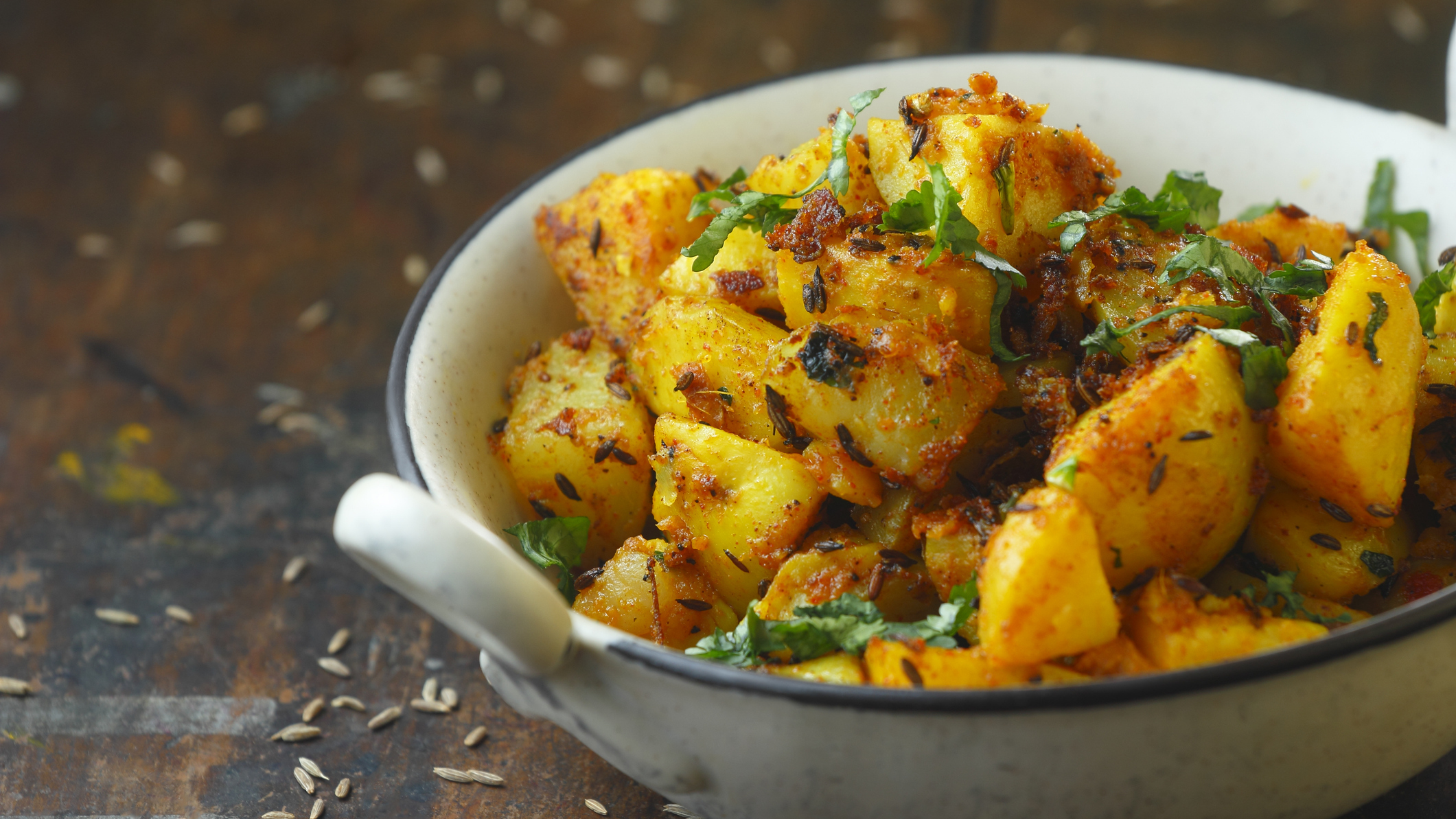 A bowl of potatoes cooked in a yellow spice and topped with a chopped green herb