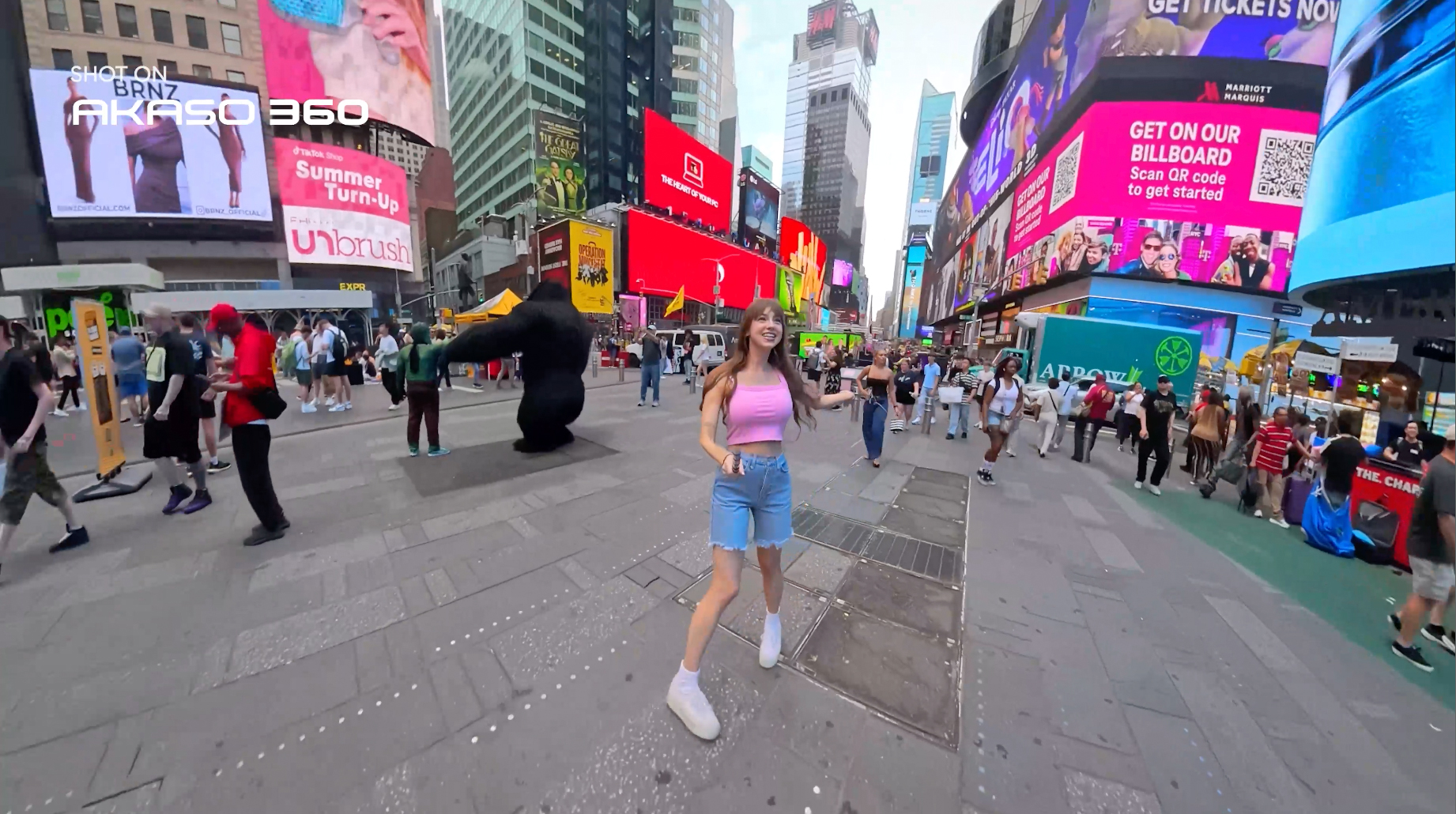 Person in pink top holding Akaso 360 camera with invisible selfie stick in public square