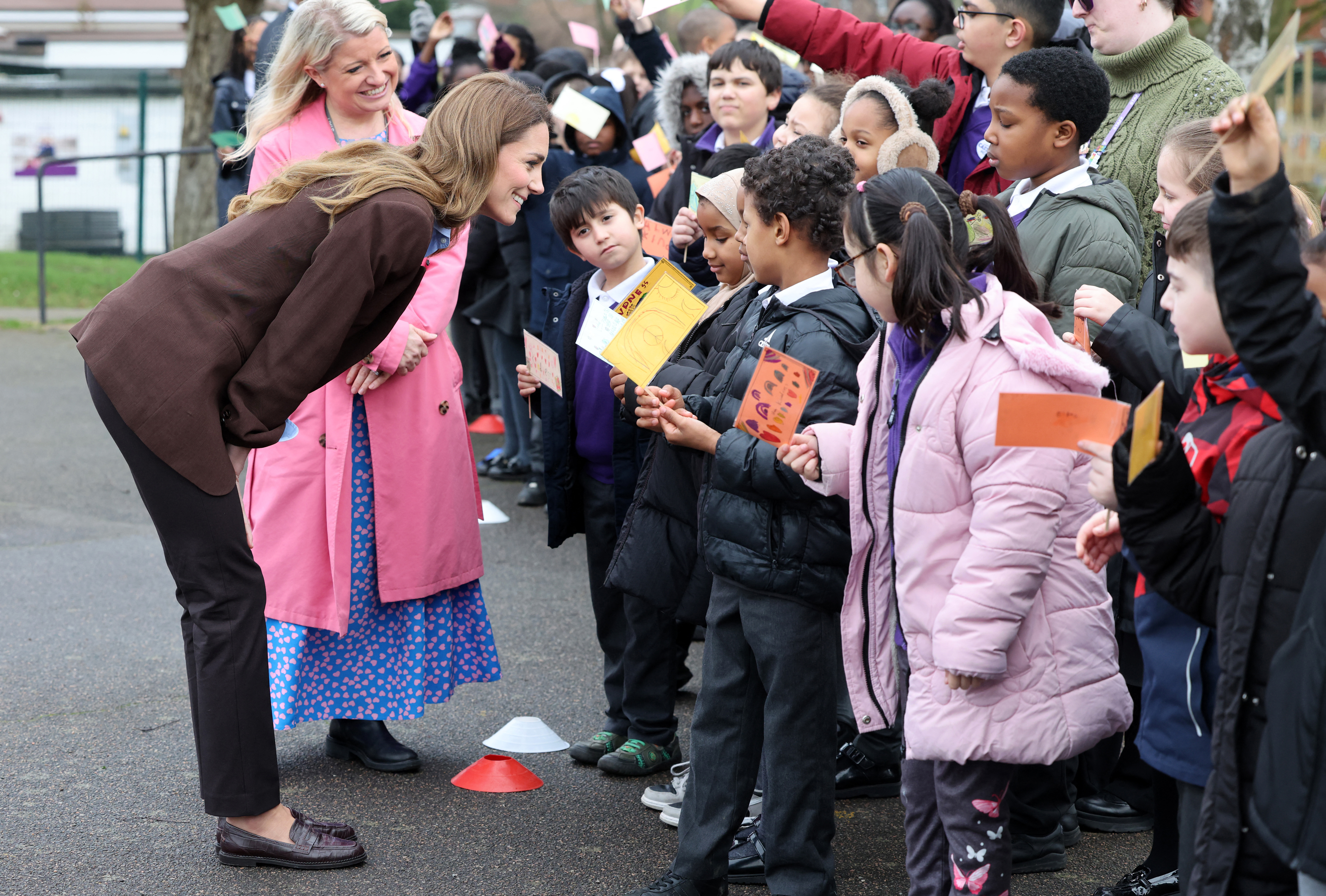 Princess Kate wearing a brown blazer leaning forward to talk to children