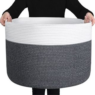 Extra large round gray and white cotton woven storage basket being held by a person in black clothing for scale. It's very large, starting at their chest, and down to their knees