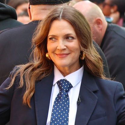 Drew Barrymore poses outside while wearing a dark blue suit with a white shirt and a blue and white polka dot tie