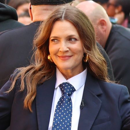 Drew Barrymore poses outside while wearing a dark blue suit with a white shirt and a blue and white polka dot tie