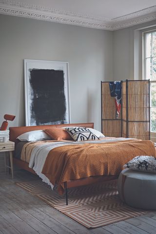 Bedroom with stripped wooden floor, elaborate coving and double bed with black, white and orange bedding