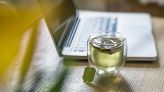 Glass cup of green tea sitting next to laptop on wooden desk
