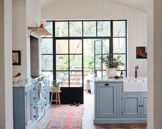 Sky blue kitchen island with sink and sky blue cabinets, and crittall doors leading to garden
