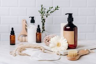 A variety of bottles of self-care essentials like face wash and body wash with face towels and exfoliating brushes in a bathroom.