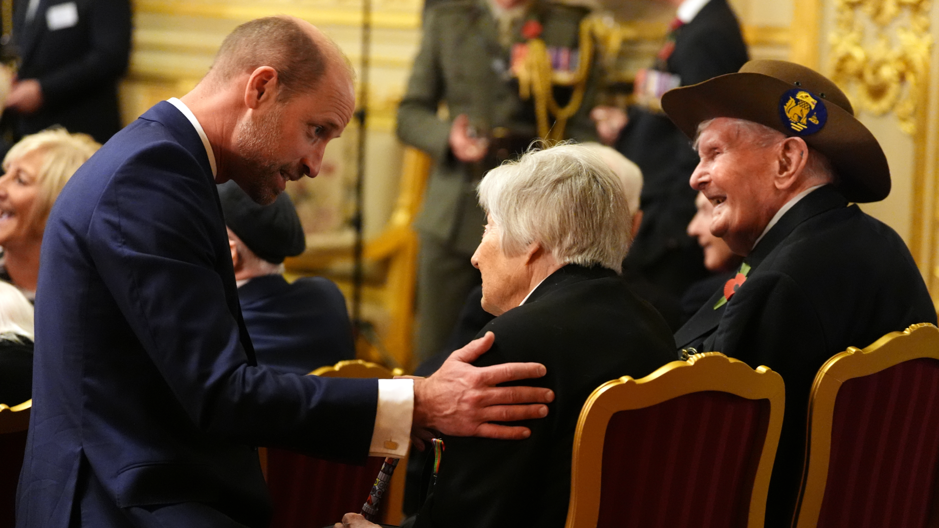 Prince William kneeling and putting his hand on an elderly woman&#039;s shoulder 
