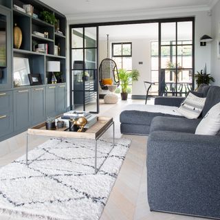 A living room with white walls and built-in charcoal grey storage with a matching sofa and a Berber-style rug on the floor