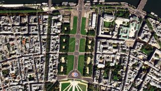 A satellite image showing green walkways surrounded by a grid of buildings, with a river at the edge