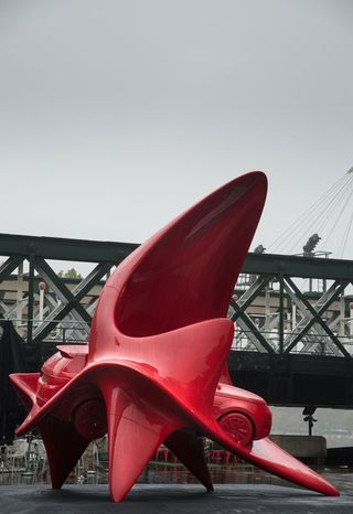 Giant red art sculpture of a land drover - side view