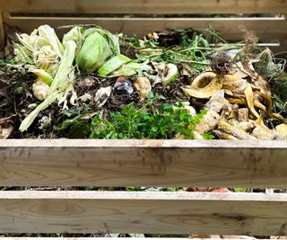 A homemade wooden compost heap full of vegetables and garden waste