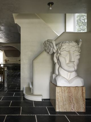 entry hallway with large black tiles, white plaster staircase and large white sculpture