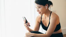 A woman practising yoga while using a phone and earbuds