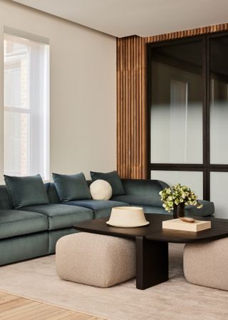 Dark blue-green corner sofa in a small living room with cream walls and slatted wooden feature