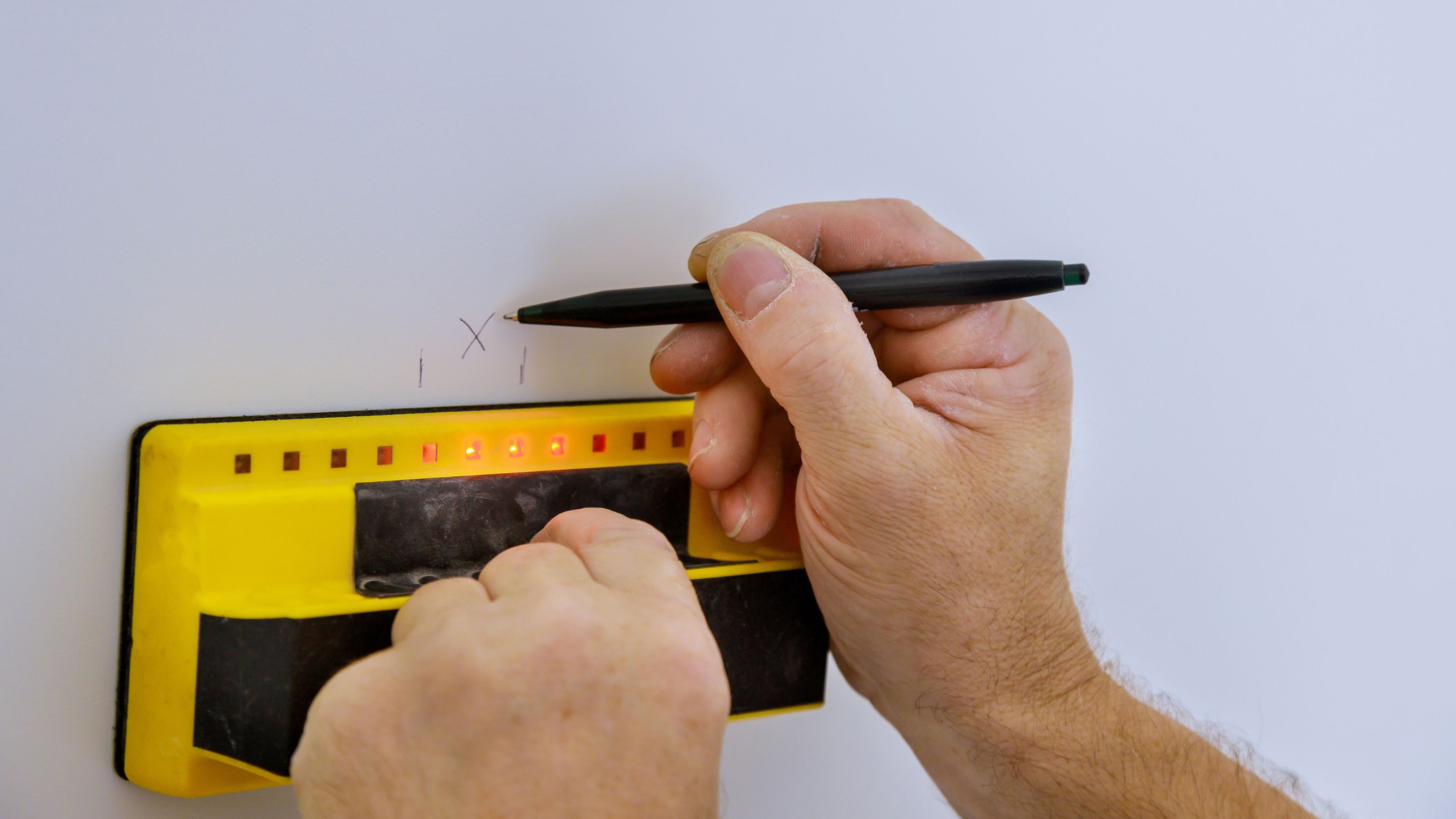 Person using a stud finder and marking the stud on the wall with a pencil