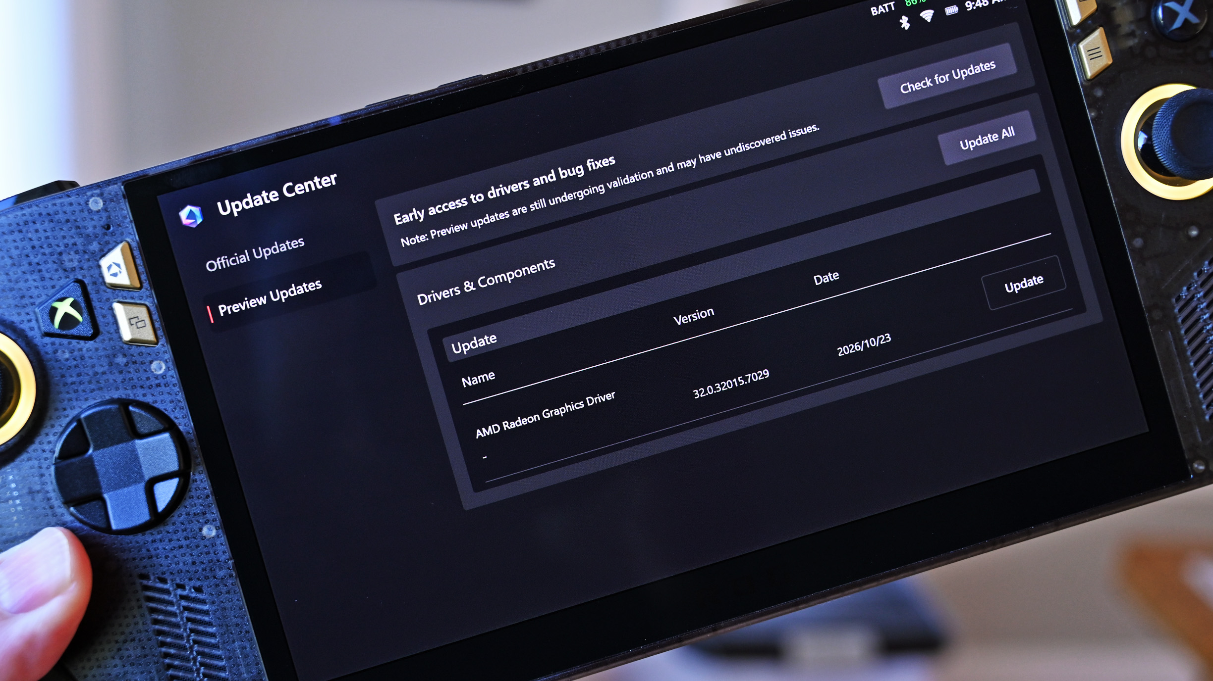 Handheld ROG Ally held in hand, displaying the Update Center screen with a preview update for the AMD Radeon Graphics Driver version 32.0.32015.7029.