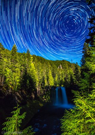 Star trails swirl over Koosah Falls in Oregon. Taken by photographer Justin Hartney, this image captures the soft flow of water cascading over the rock cliffs. The moonlight illuminates the surrounding trees, giving them a bright green glow.