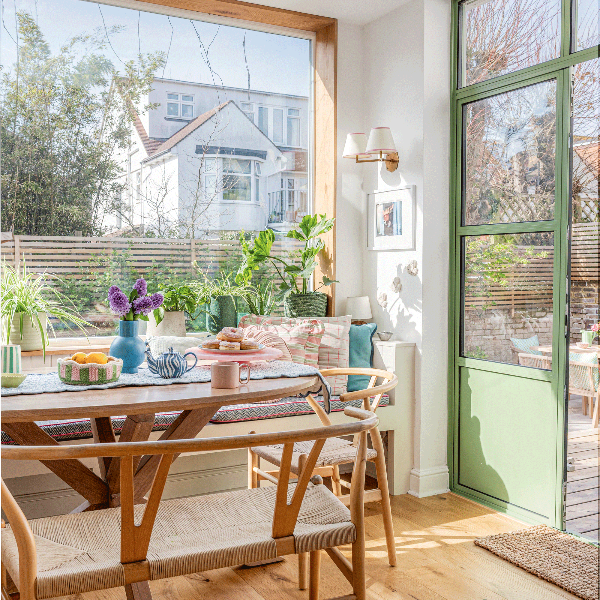 an open-plan kitchen diner with wishbone chairs and a bench, green patio doors, banquette seating and a large picture window facing the garden