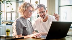 Looking at Roth IRA options, an older couple at home work together on a laptop computer.