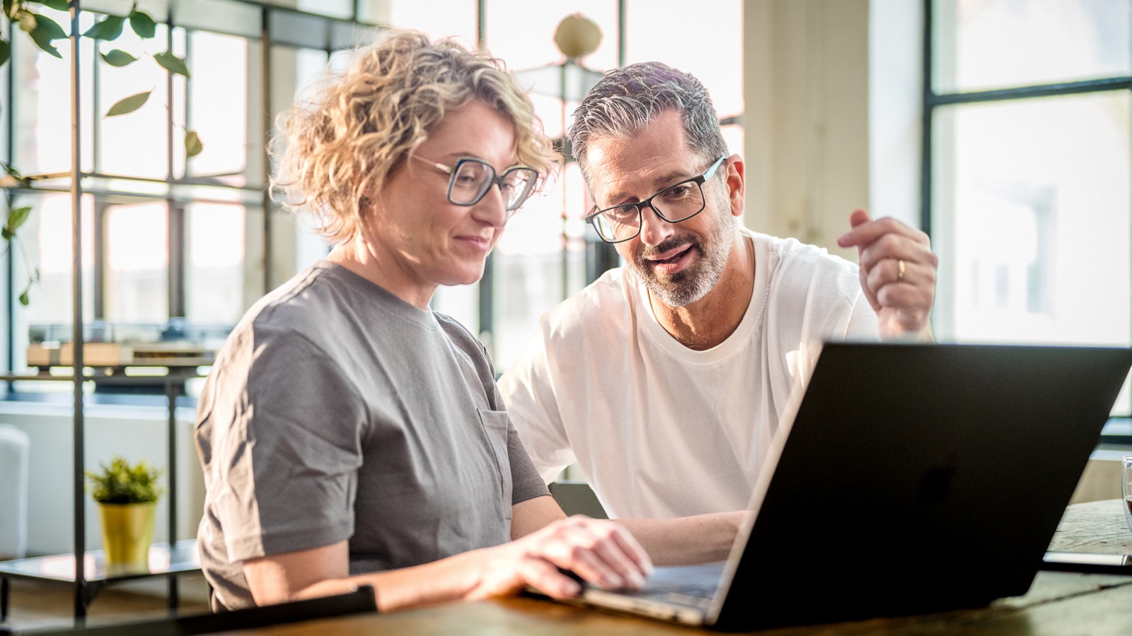 Looking at Roth IRA options, an older couple at home work together on a laptop computer. 