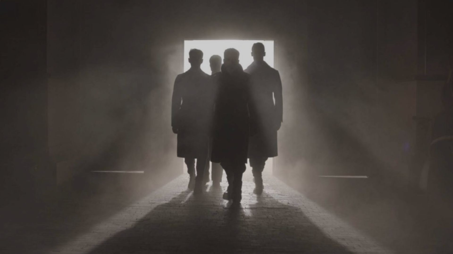 an image of four men completely in shadow, standing in the entrance of a warehouse, backlit by a single light so you cannot see faces, only silhouettes