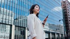 A successful woman holds a cellphone in front of an office building.