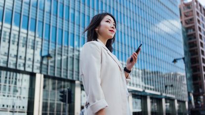 A successful woman holds a cellphone in front of an office building.