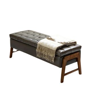 A leather storage bench with wooden legs and a folded blanket on top