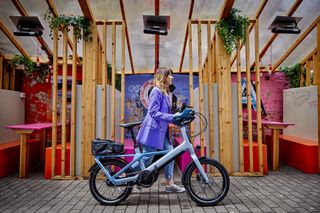 A woman wheeling a Raleigh Modum e-bike through an outdoor dining area