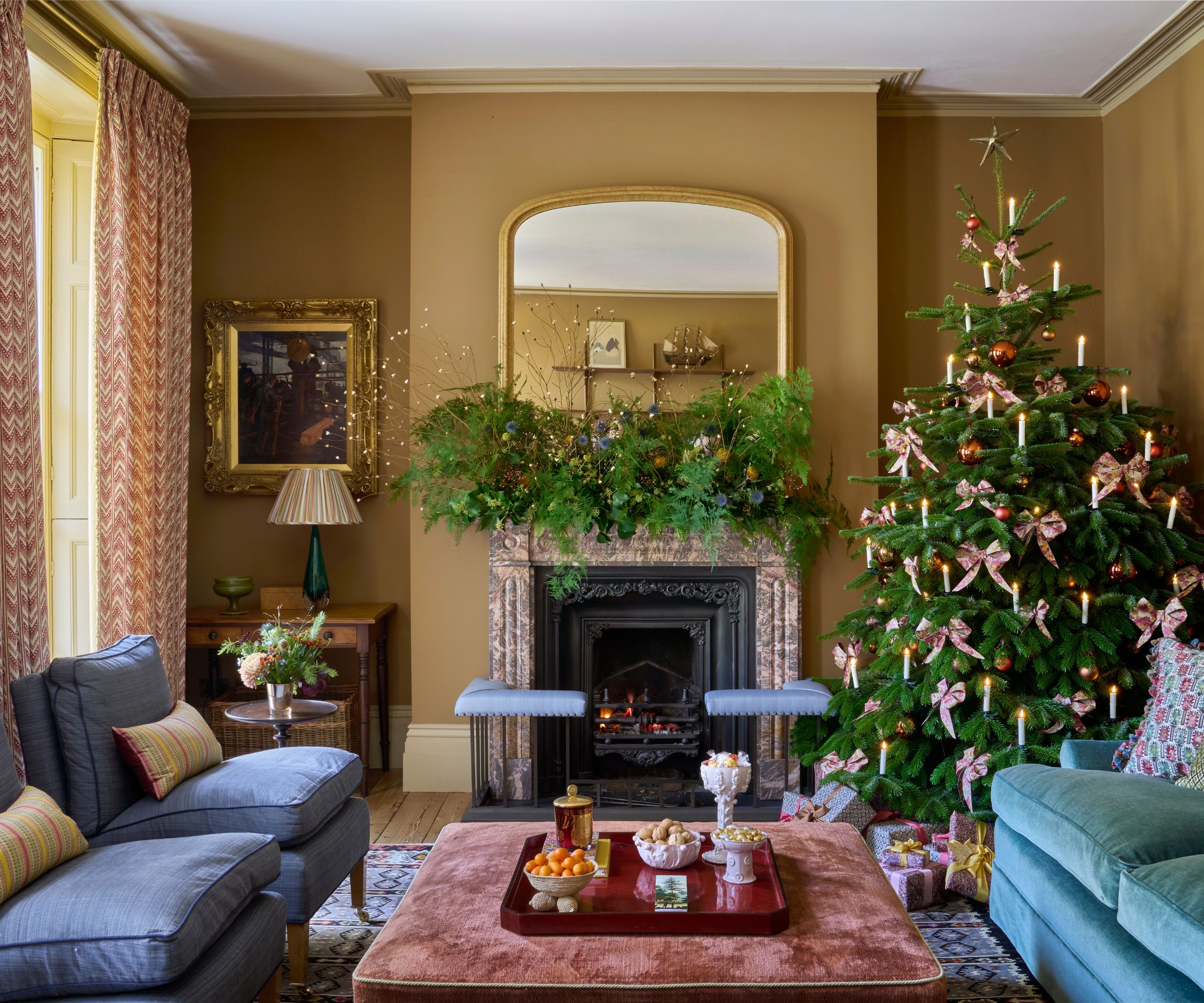 Yellow living room decorated for Christmas with a tree decorated with bows in one corner and blue seating