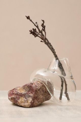 A clear glass vase that's blown around the rock in red and brown tones. There are tree branches in the vase.