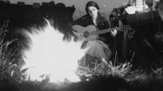 Valerie White and Betty Redshaw singing and playing the guitar outside their tent in the Gloucestershire countryside. They have been busking around the English countryside making money to extend their summer holiday. Original Publication: Picture Post - 6827 - Summer Catches Up On Us - pub. 1953