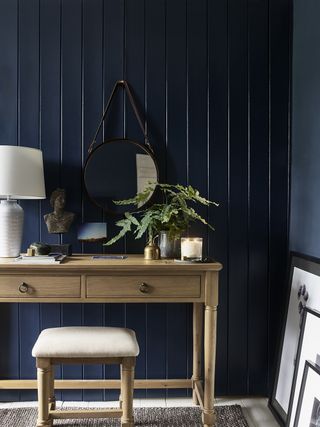 Navy blue shiplap paneling in a bedroom with a wooden dressing table and seat