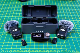 A photo of the DJI Mic 2 (TX/RX/charging case) open and laid out on a green and yellow cutting mat.