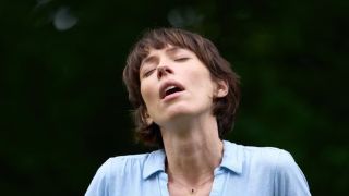 A ecstatic-looking Claire (Rebecca Hall) sands outside in a blue shirt, experiencing a humming sound very few can hear in new BBC drama The Listeners