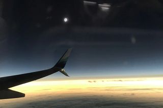 view of a solar eclipse in the distance over clouds and a plane's wing