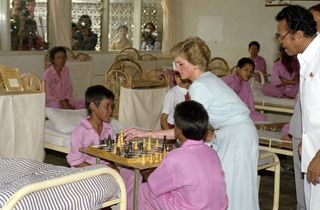 Princess Diana wearing a blue dress playing chess with children in a hospital