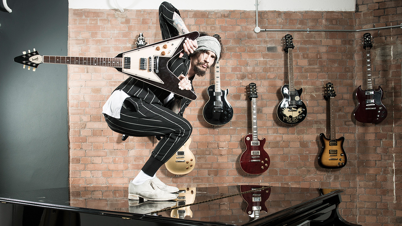 a shot of Justin Hawkins crouching on a grand piano holding a guitar