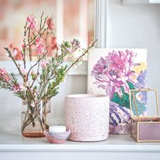 Two candles on a white worktop with a pink vase and fresh flowers