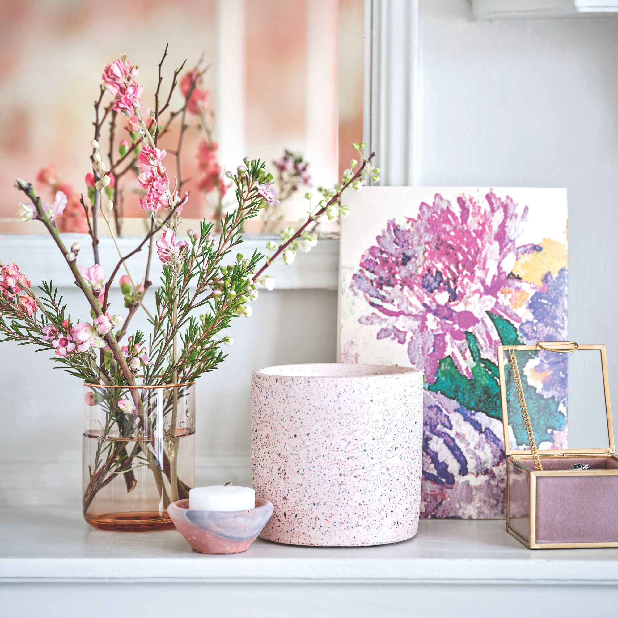 Two candles on a white worktop with a pink vase and fresh flowers