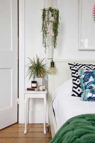 a white bedroom with a green throw on bed and hanging plant