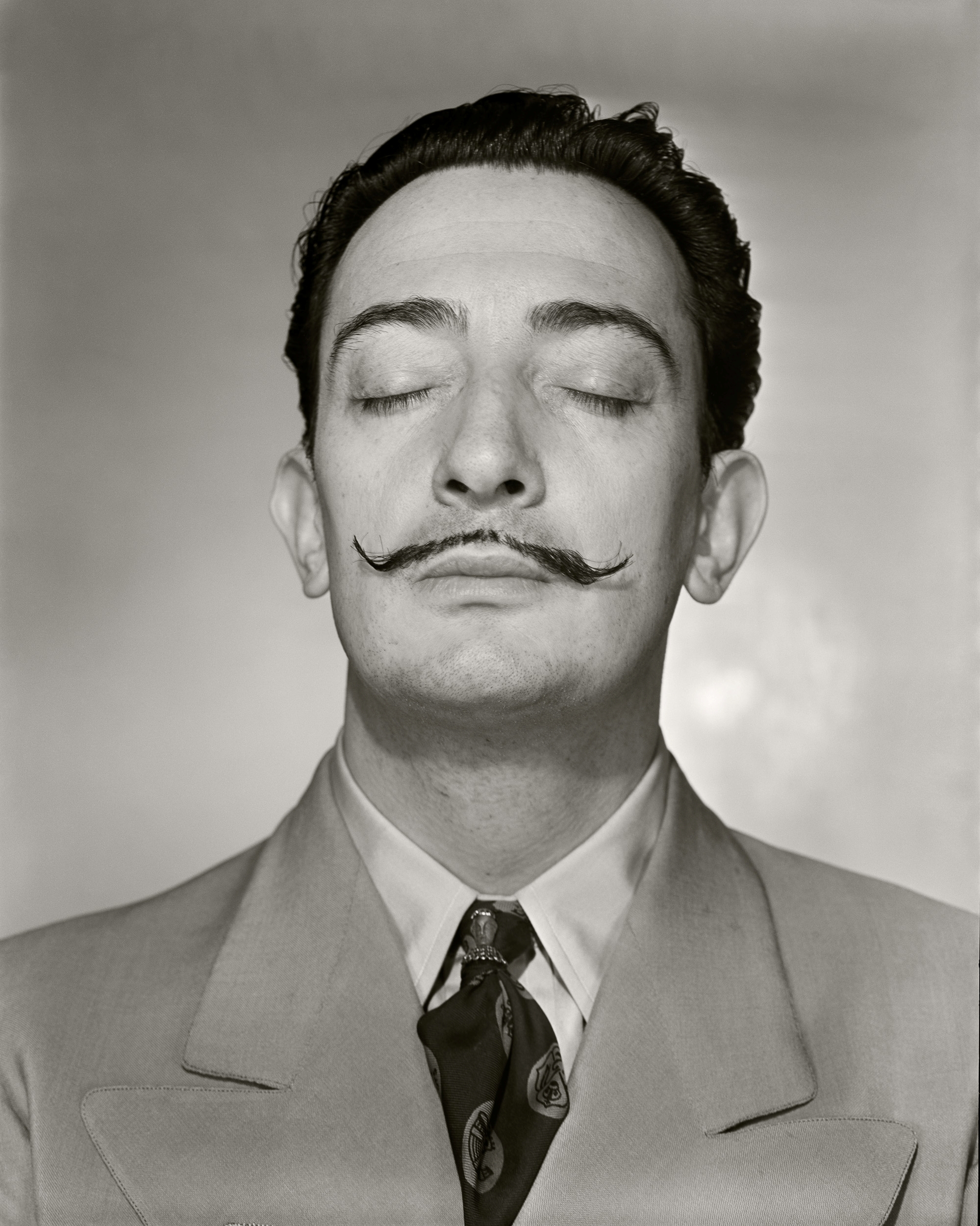 A symmetrical, close-up portrait shows the artist Salvador Dal&amp;iacute; with his eyes closed and his signature waxed mustache perfectly styled.