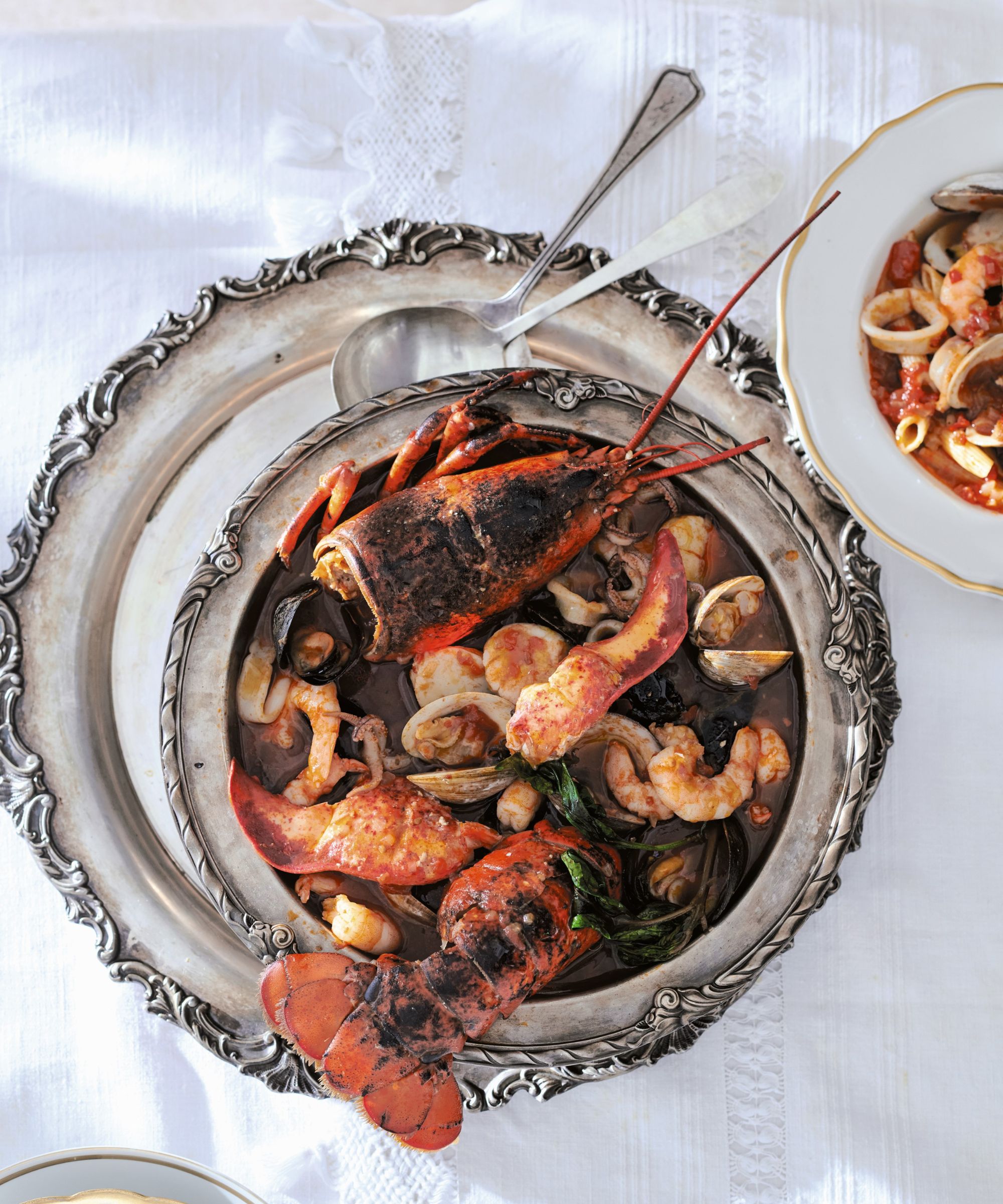 Bowl of seafood stew with lobster tail on silver plates