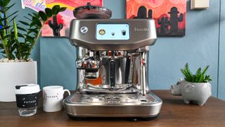 A front-on view of the Breville Oracle Jet coffee machine sitting on a dark wooden table with decorative plants to either side.