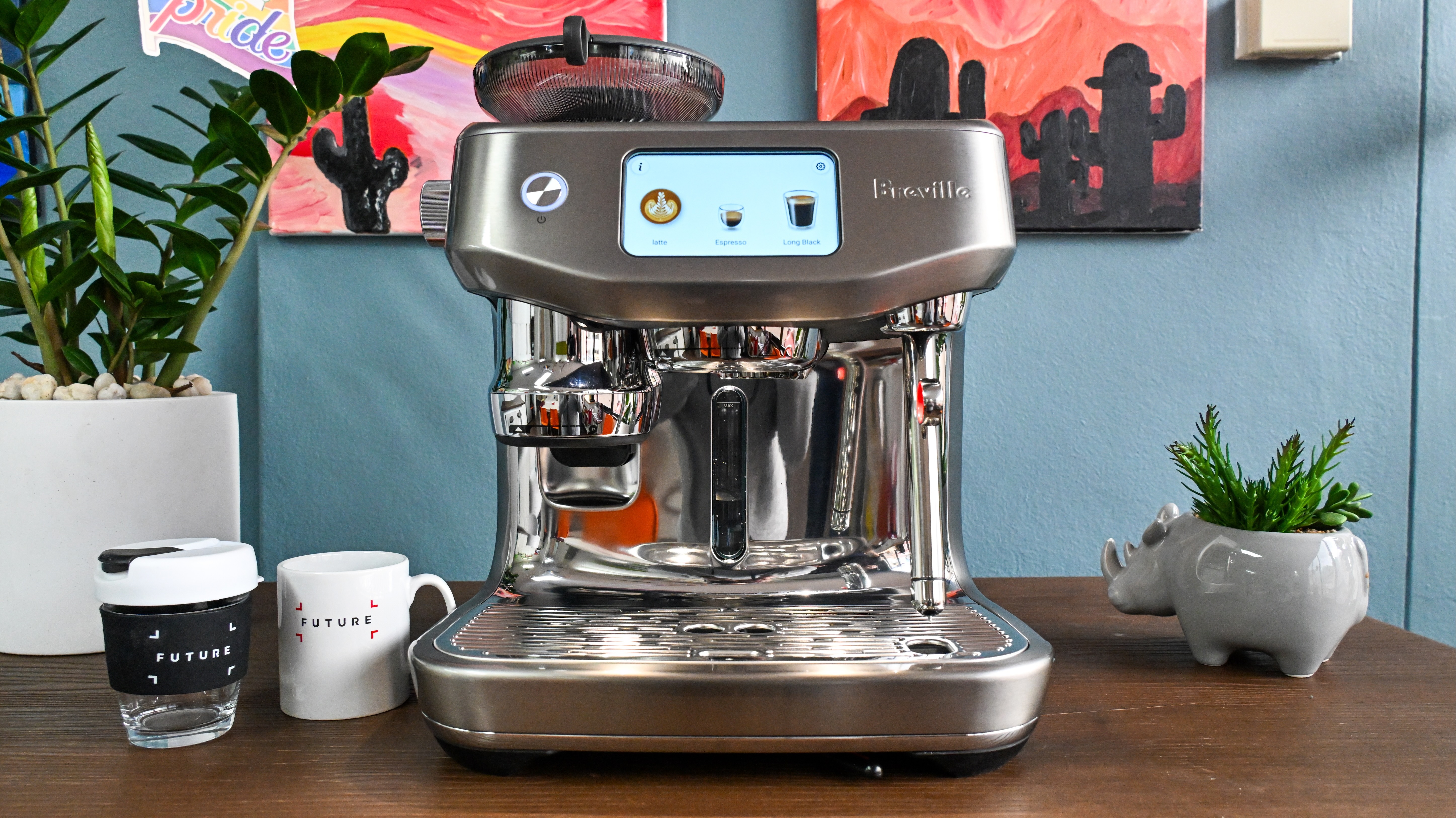 A front-on view of the Breville Oracle Jet coffee machine sitting on a dark wooden table with decorative plants to either side.