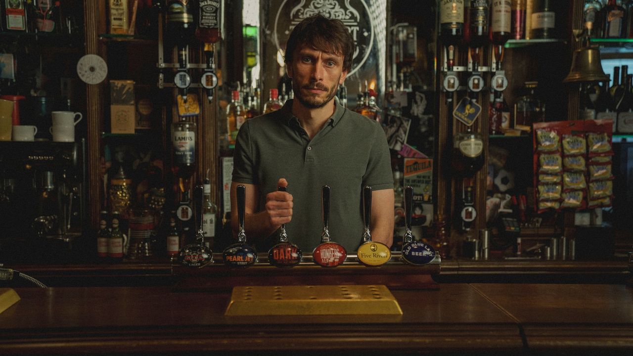 a man (richard Gadd as donny dunn) stands behind a bar with his hand on a tap handle, in netflix&#039;s &#039;baby reindeer&#039;