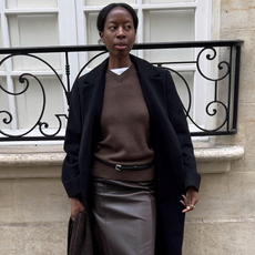 Influencer Sylvie Mus wearing brown cashmere sweater, white t-shirt, black coat, and grey skirt in Paris.