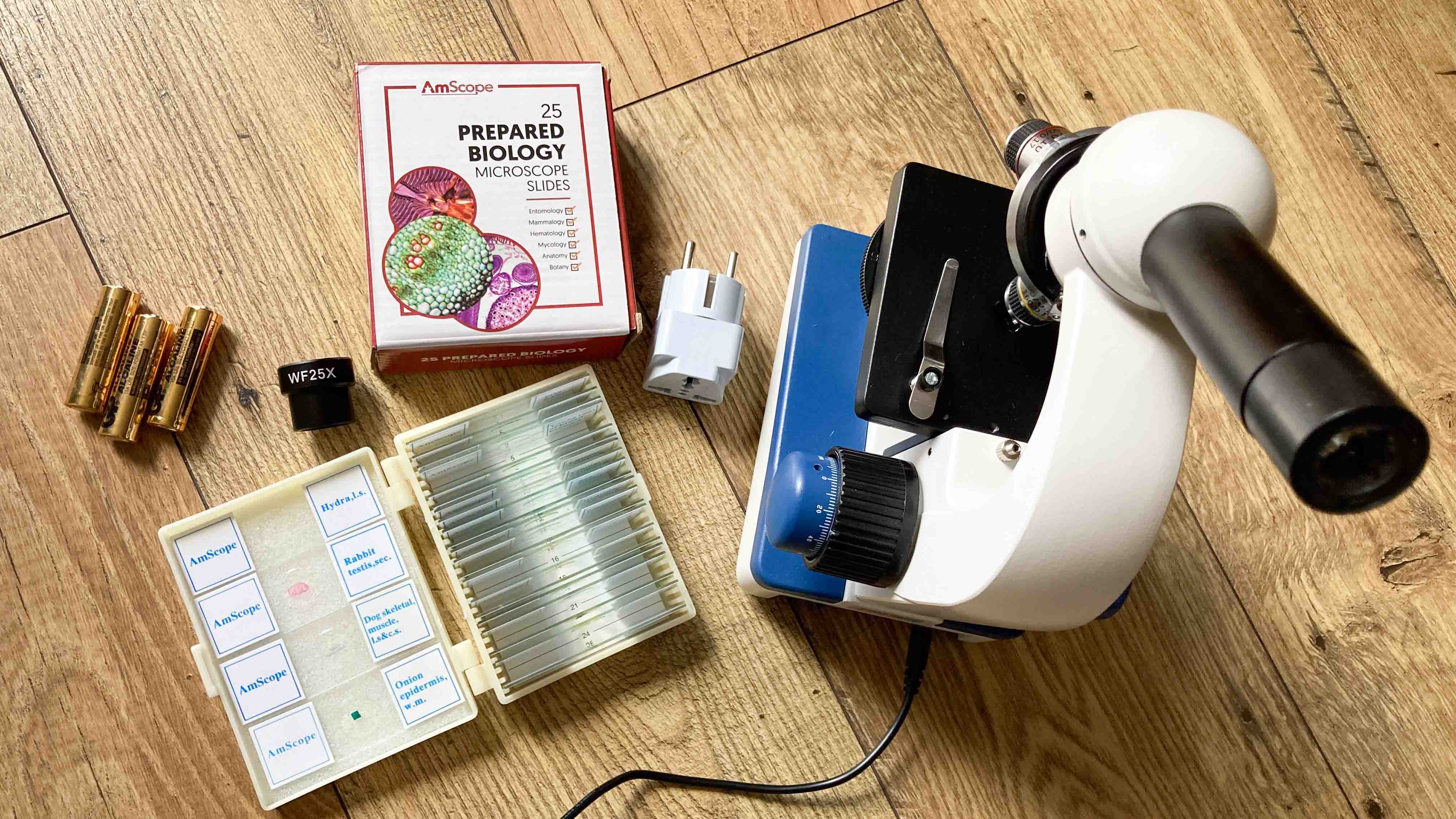 Microscope and the prepared slides that ship with the product laid out on a wooden table with a top-down view