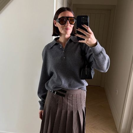 a woman wearing a gray sweater, a kilt plaid skirt, and round black sunglasses